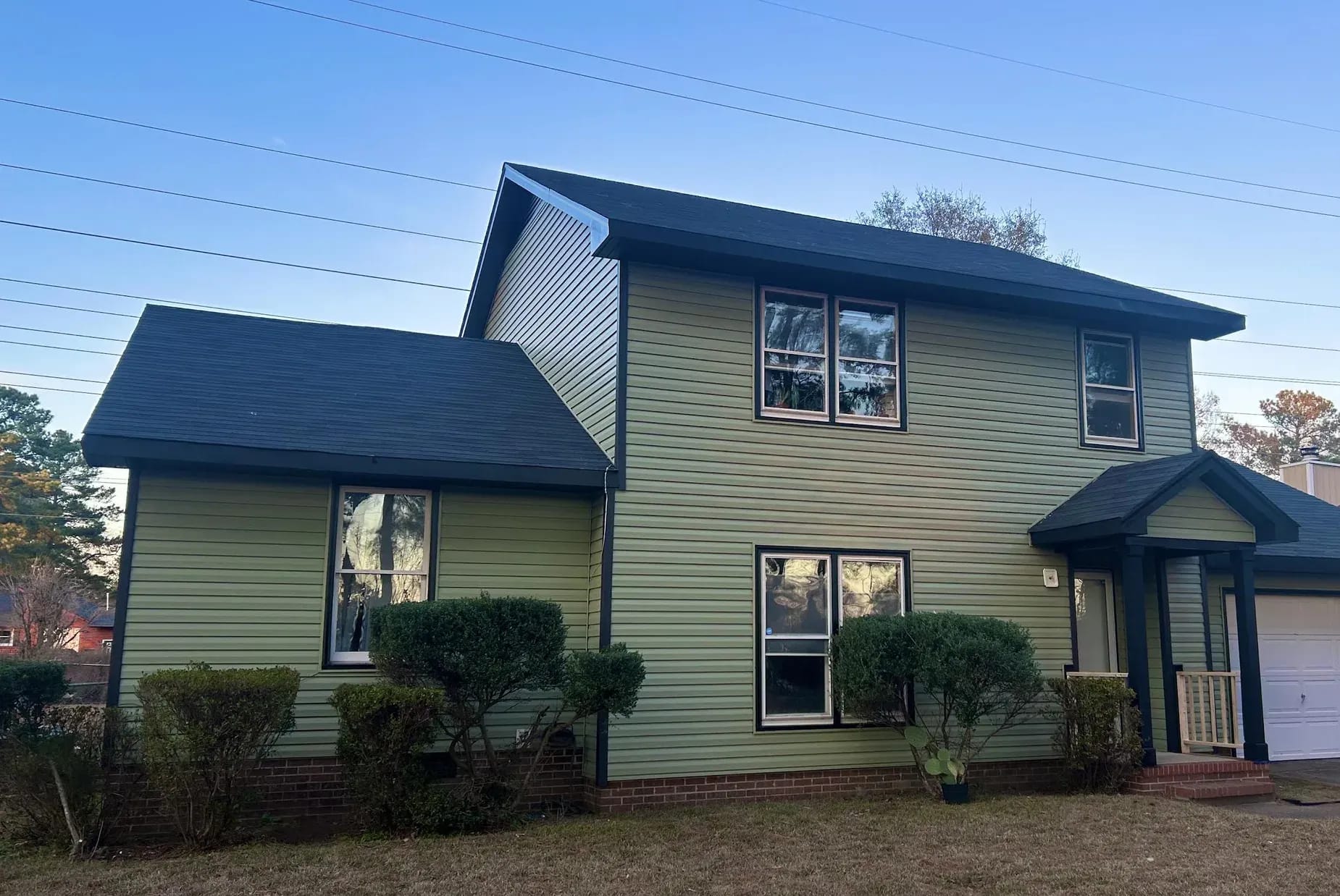 The same home renewed in sage green siding with dark trim around the windows and porch.