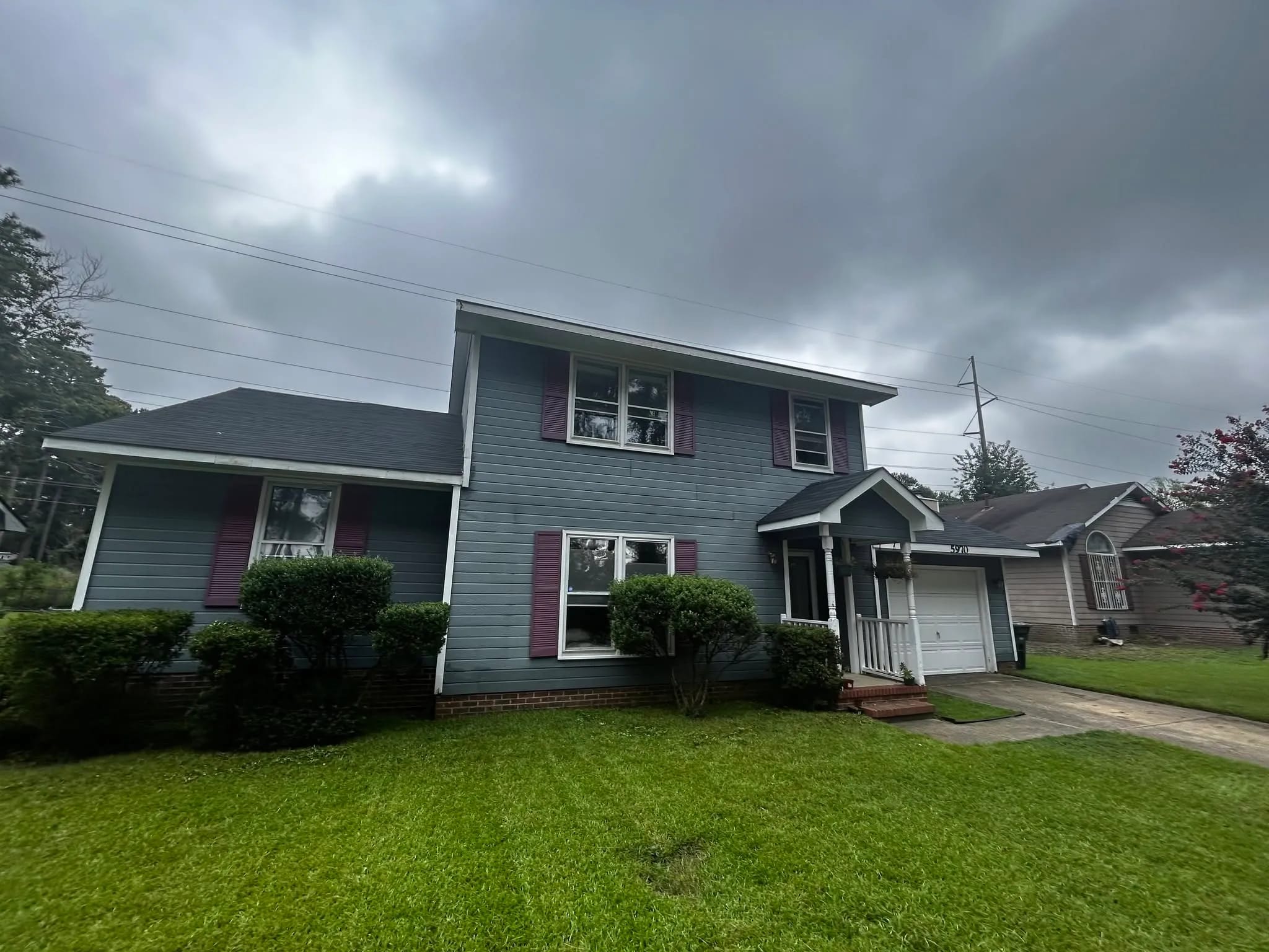 Two-storey home with faded grey siding and burgundy shutters under a cloudy sky, before its renewal.