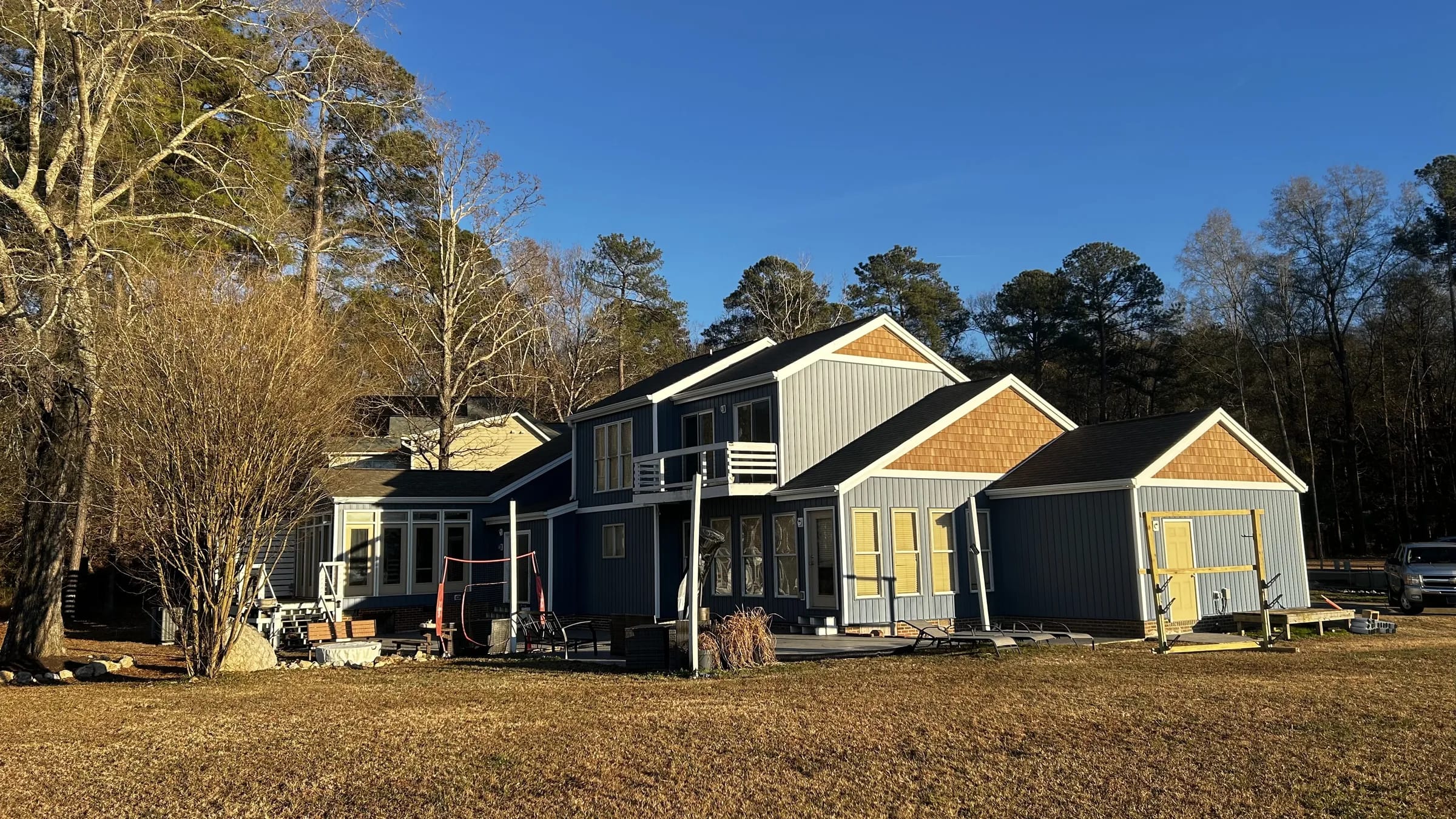Wide view of a finished home with blue-gray siding, white trim and warm shingle gables beneath a clear sky.