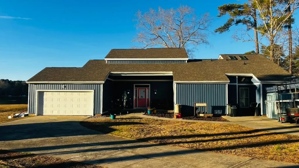 Low, wide home in blue-gray vertical siding with white trim, a red front door and a white garage door, under a clear blue sky.