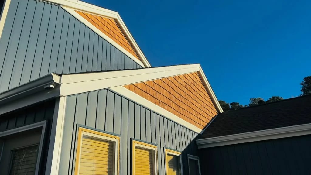 Blue-gray vertical siding meeting cedar-toned shingle gables and white trim, against a deep blue sky.